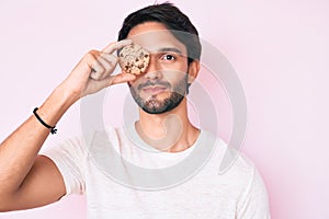 Handsome hispanic man holding cookie thinking attitude and sober expression looking self confident