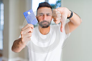 Handsome hispanic man holding credit card with angry face, negative sign showing dislike with thumbs down, rejection concept