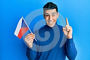Handsome hispanic man holding czech republic flag smiling with an idea or question pointing finger with happy face, number one