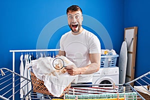 Handsome hispanic man holding magnifying glass looking for stain at clothes celebrating crazy and amazed for success with open