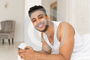 Handsome Hispanic Man Lying In Bed Using Cell Smart Phone, Young Guy Happy Smile