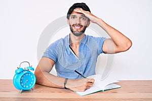 Handsome hispanic man sitting on the table stuying for university stressed and frustrated with hand on head, surprised and angry