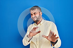 Handsome hispanic man standing over blue background disgusted expression, displeased and fearful doing disgust face because