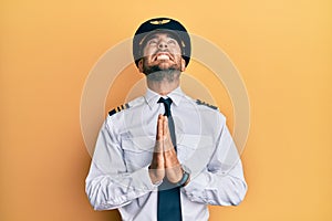 Handsome hispanic man wearing airplane pilot uniform begging and praying with hands together with hope expression on face very