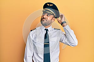 Handsome hispanic man wearing airplane pilot uniform confuse and wondering about question