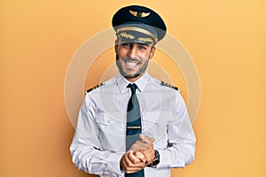 Handsome hispanic man wearing airplane pilot uniform with hands together and crossed fingers smiling relaxed and cheerful