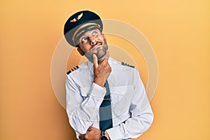 Handsome hispanic man wearing airplane pilot uniform thinking worried about a question, concerned and nervous with hand on chin