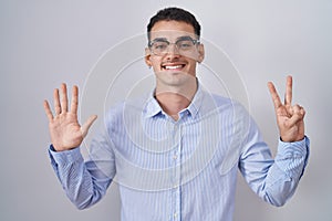 Handsome hispanic man wearing business clothes and glasses showing and pointing up with fingers number seven while smiling