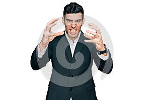 Handsome hispanic man wearing business clothes shouting frustrated with rage, hands trying to strangle, yelling mad