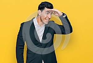 Handsome hispanic man wearing business clothes very happy and smiling looking far away with hand over head