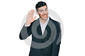 Handsome hispanic man wearing business clothes waiving saying hello happy and smiling, friendly welcome gesture