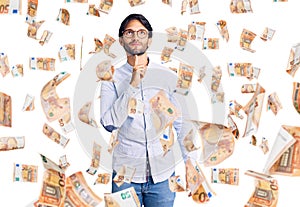 Handsome hispanic man wearing business shirt and glasses thinking concentrated about doubt with finger on chin and looking up