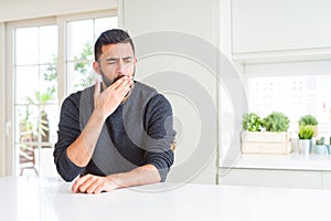 Handsome hispanic man wearing casual sweater at home bored yawning tired covering mouth with hand