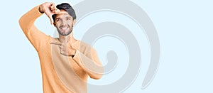 Handsome hispanic man wearing casual sweater smiling making frame with hands and fingers with happy face