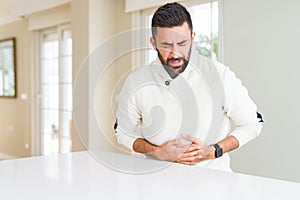 Handsome hispanic man wearing casual white sweater at home with hand on stomach because indigestion, painful illness feeling