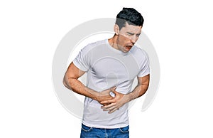 Handsome hispanic man wearing casual white t shirt with hand on stomach because nausea, painful disease feeling unwell