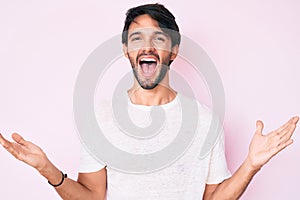 Handsome hispanic man wearing casual white tshirt celebrating victory with happy smile and winner expression with raised hands