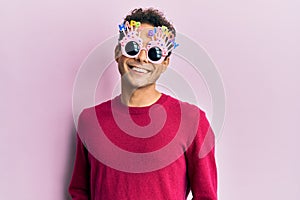 Handsome hispanic man wearing funny happy birthday glasses with a happy and cool smile on face