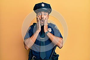 Handsome hispanic man wearing police uniform afraid and shocked, surprise and amazed expression with hands on face