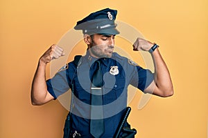Handsome hispanic man wearing police uniform showing arms muscles smiling proud