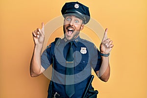 Handsome hispanic man wearing police uniform smiling amazed and surprised and pointing up with fingers and raised arms