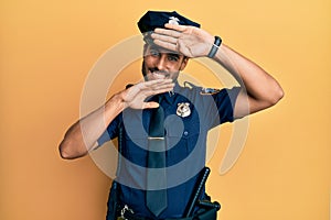 Handsome hispanic man wearing police uniform smiling cheerful playing peek a boo with hands showing face