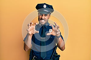 Handsome hispanic man wearing police uniform smiling funny doing claw gesture as cat, aggressive and sexy expression