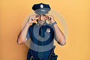 Handsome hispanic man wearing police uniform trying to open eyes with fingers, sleepy and tired for morning fatigue