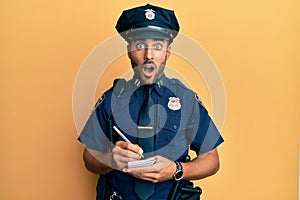 Handsome hispanic man wearing police uniform writing traffic fine afraid and shocked with surprise and amazed expression, fear and