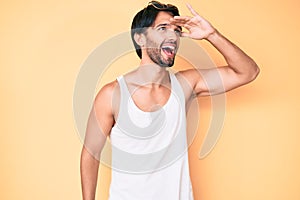 Handsome hispanic man wearing summer look and sunglasses very happy and smiling looking far away with hand over head