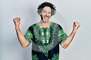 Handsome hispanic man wearing traditional african clothes screaming proud, celebrating victory and success very excited with