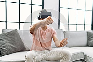 Handsome hispanic man wearing virtual reality glasses driving on videogame at the living room at home