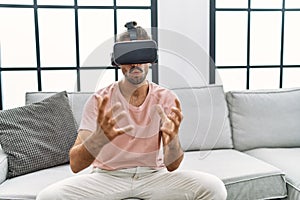 Handsome hispanic man wearing virtual reality glasses at the living room at home