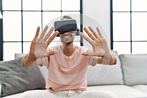 Handsome hispanic man wearing virtual reality glasses at the living room at home