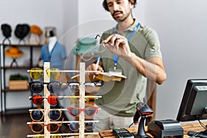 Handsome hispanic man working as shop assistance holding glasses at retail shop