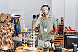 Handsome hispanic man working as shop assistance speaking on the phone at retail shop