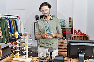 Handsome hispanic man working as shop assistance using smartphone at retail shop