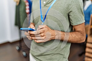 Handsome hispanic man working as shop assistance using smartphone at retail shop