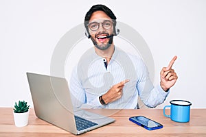 Handsome hispanic man working at the office wearing operator headset smiling and looking at the camera pointing with two hands and