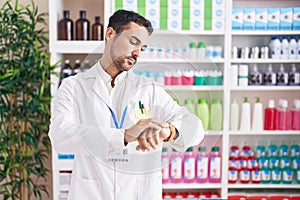 Handsome hispanic man working at pharmacy drugstore checking the time on wrist watch, relaxed and confident