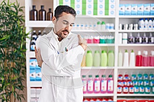 Handsome hispanic man working at pharmacy drugstore hugging oneself happy and positive, smiling confident