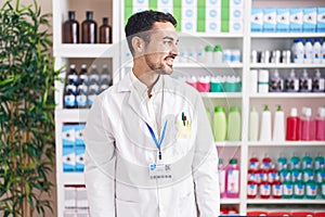 Handsome hispanic man working at pharmacy drugstore looking away to side with smile on face, natural expression