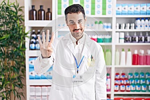 Handsome hispanic man working at pharmacy drugstore showing and pointing up with fingers number four while smiling confident and