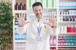 Handsome hispanic man working at pharmacy drugstore showing and pointing up with fingers number ten while smiling confident and