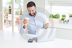 Handsome hispanic man working using computer laptop and drinking a cup of coffee screaming proud and celebrating victory and