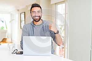 Handsome hispanic man working using computer laptop happy with big smile doing ok sign, thumb up with fingers, excellent sign