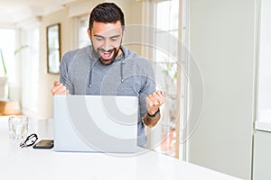 Handsome hispanic man working using computer laptop screaming proud and celebrating victory and success very excited, cheering photo