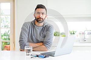 Handsome hispanic man working using computer laptop skeptic and nervous, disapproving expression on face with crossed arms