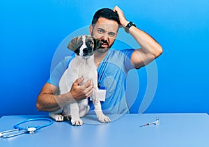 Handsome hispanic veterinary man with beard checking dog health confuse and wondering about question