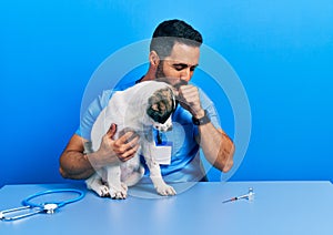 Handsome hispanic veterinary man with beard checking dog health feeling unwell and coughing as symptom for cold or bronchitis